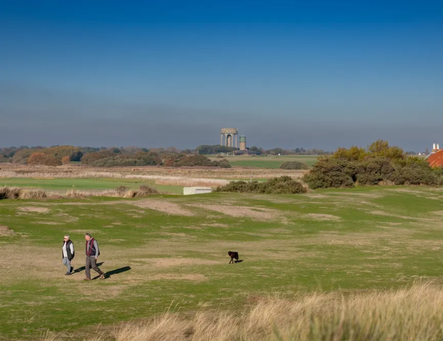 A couple walking across a sprawling field with their black dog