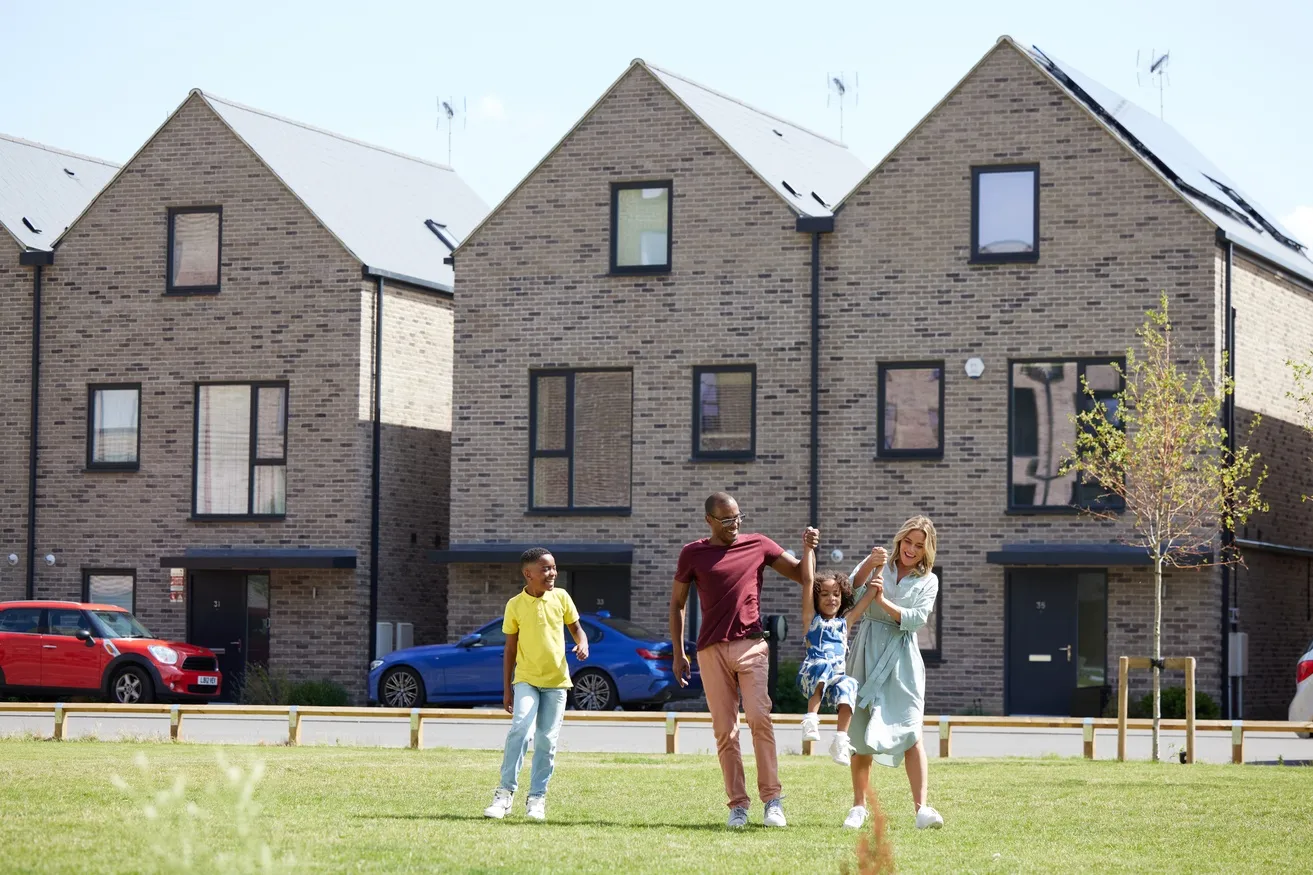 Family with two children playing on a green space in front of new build home